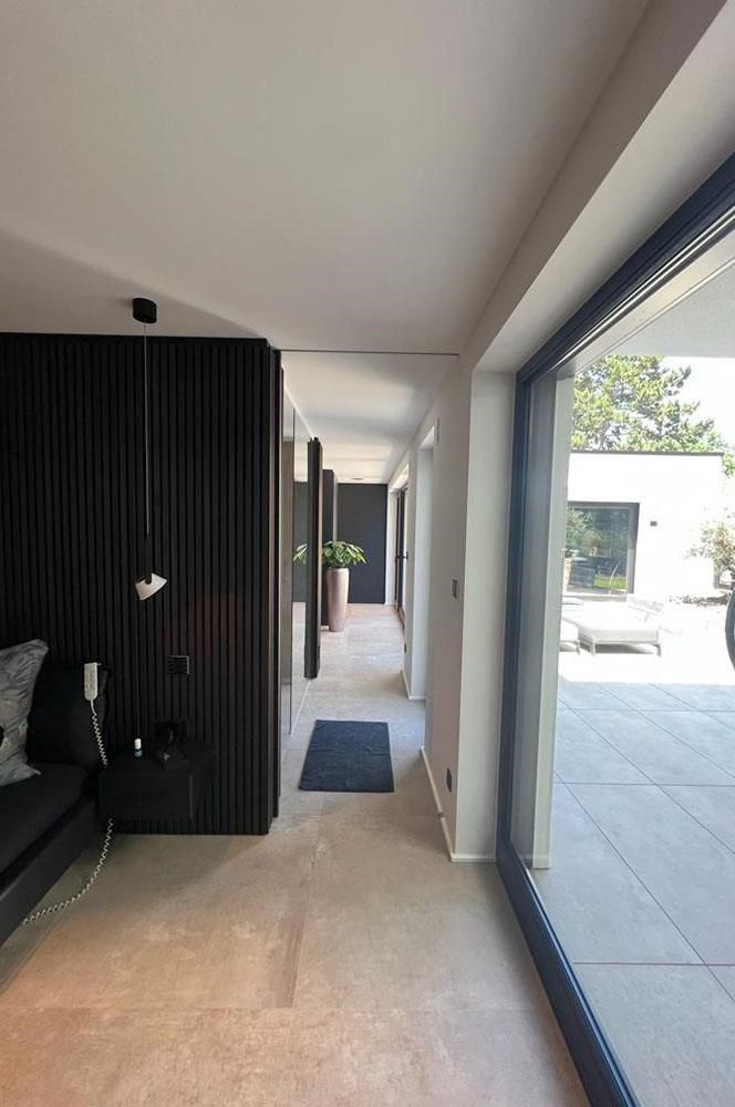 Ein langer Flur in einem Haus mit einer Glasschiebetür, die auf eine Terrasse führt.