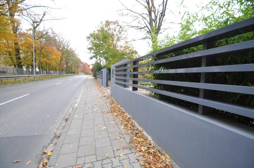 Ein Zaun am Straßenrand mit Blättern auf dem Gehweg