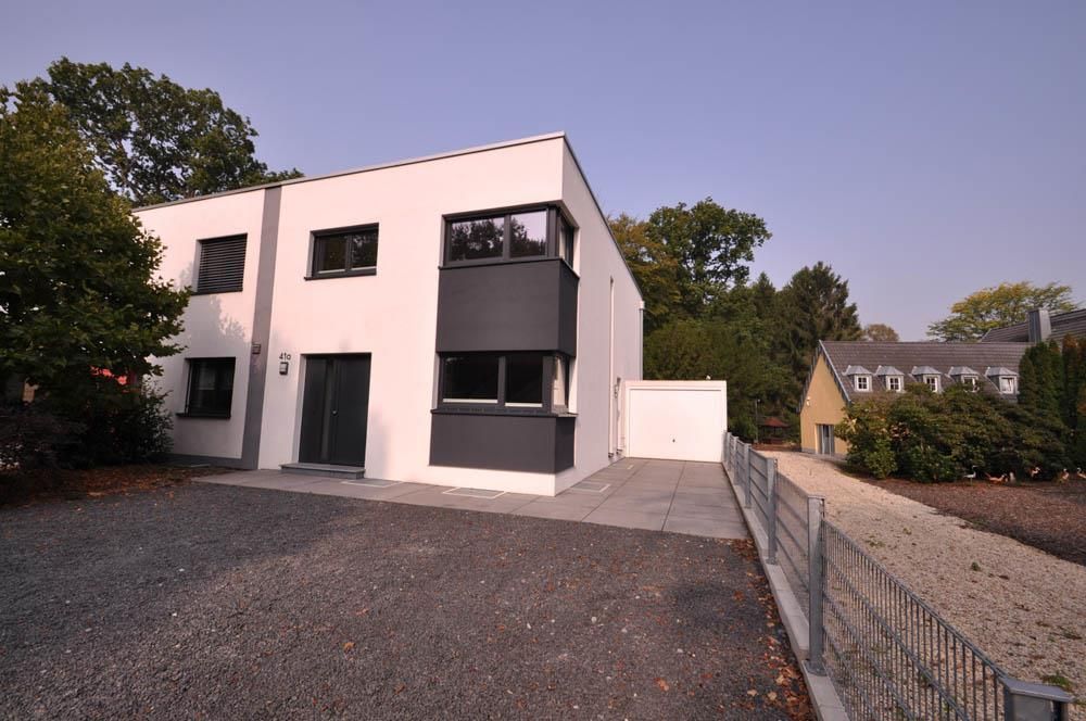 Ein weißes Haus mit Garage ist von Kies und Bäumen umgeben