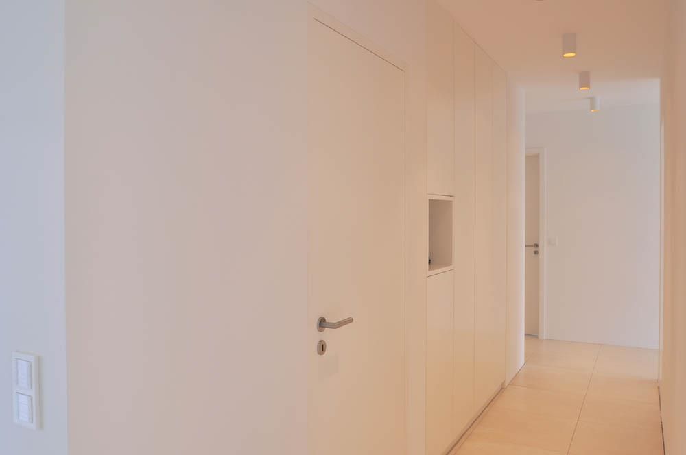 Ein langer Flur mit weißen Schränken und einer Tür in einem Haus.