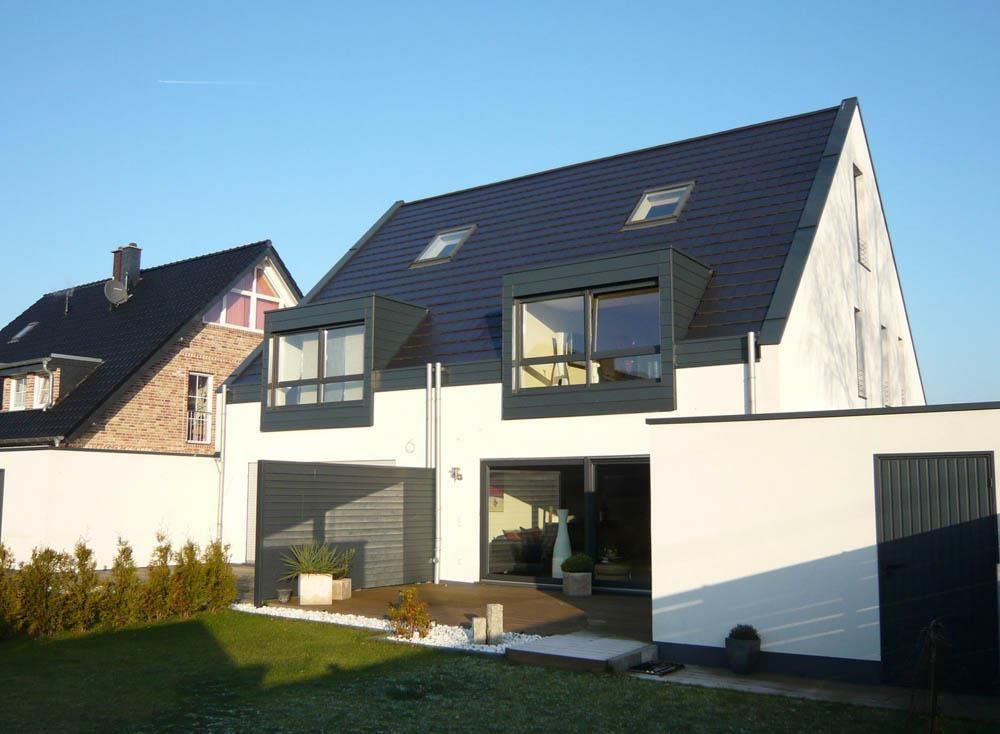 Ein weißes Haus mit schwarzem Dach steht neben einem Backsteinhaus