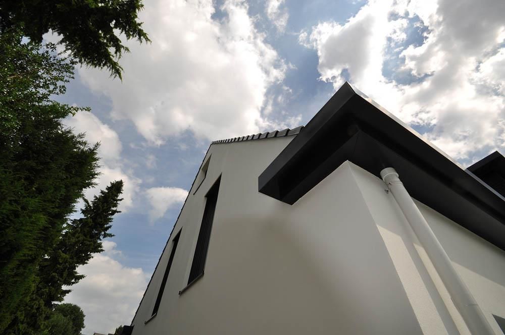 Ein weißes Haus mit einer schwarzen Dachrinne vor einem bewölkten Himmel