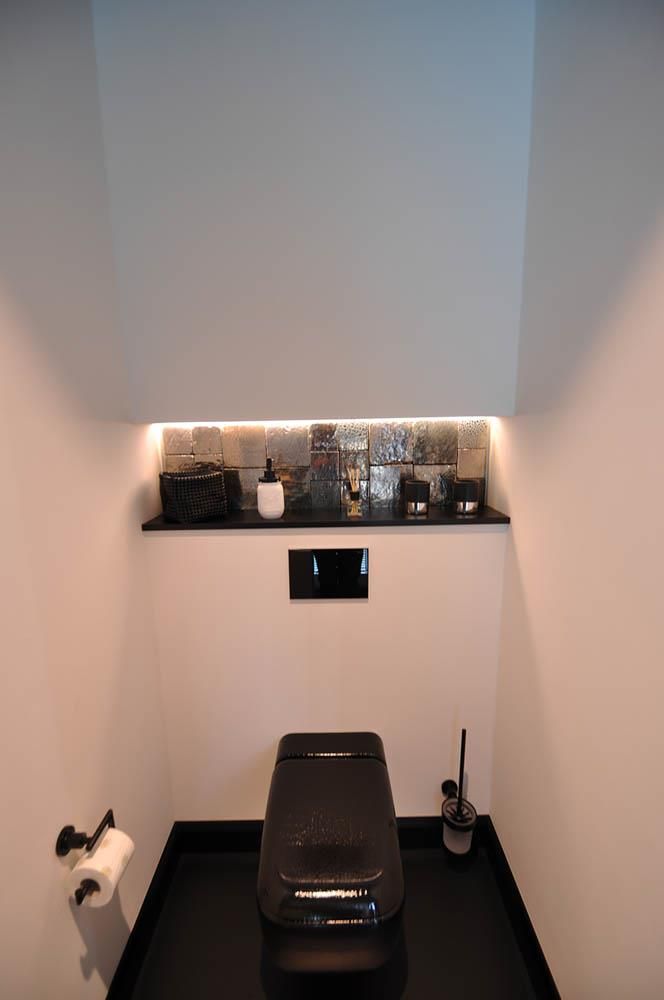 Ein Badezimmer mit einer schwarzen Toilette und einem Regal darüber