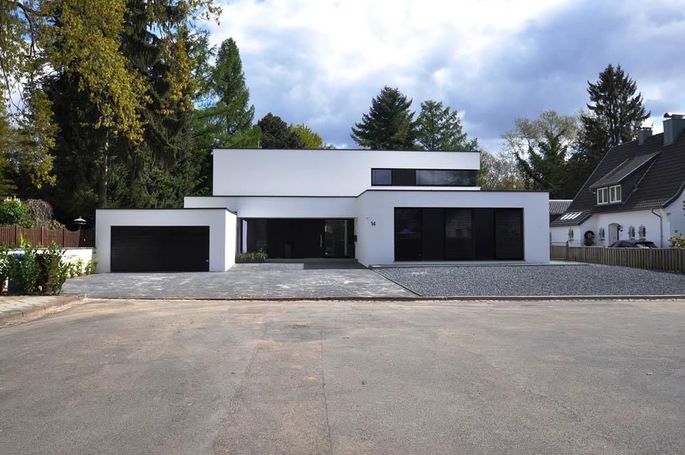 Ein weißes Haus mit schwarzen Garagentoren ist von Bäumen umgeben