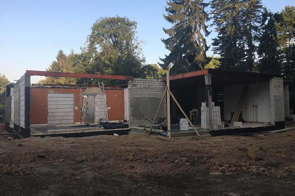 Auf einem Feld mit Bäumen im Hintergrund wird ein Haus gebaut