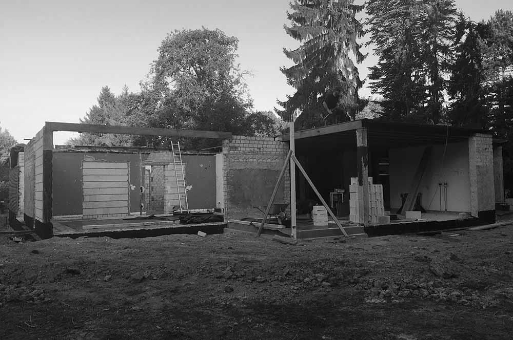 Auf einem Feld mit Bäumen im Hintergrund wird ein Haus gebaut
