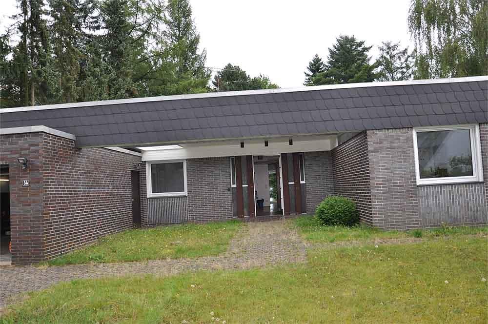 Ein Backsteinhaus mit Schieferdach ist von Gras und Bäumen umgeben.