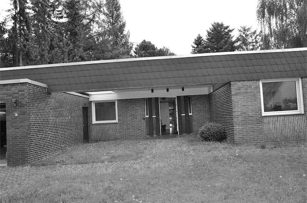 Ein Backsteinhaus mit Schieferdach ist von Gras und Bäumen umgeben.