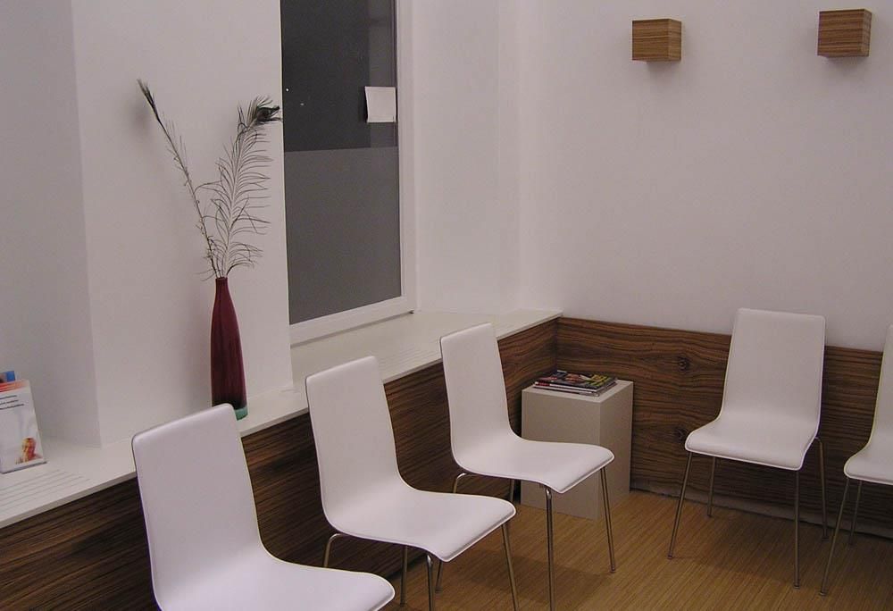 Ein Wartezimmer mit weißen Stühlen und einer Vase auf der Fensterbank
