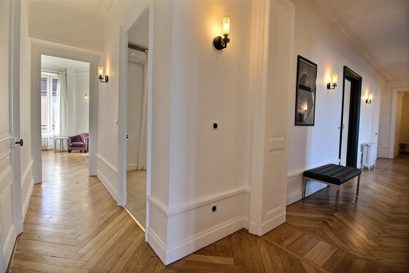 Un couloir avec un parquet et un mur blanc avec des moulures.
