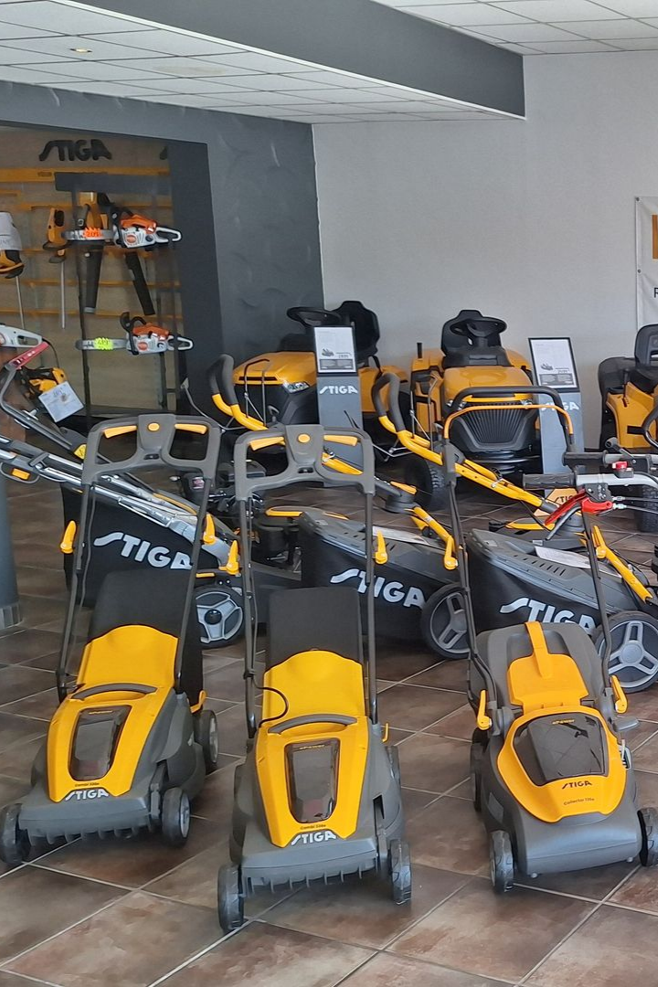 Tondeuses à gazon Stiga jaunes et grises et autres outils de jardinage exposés dans un magasin.