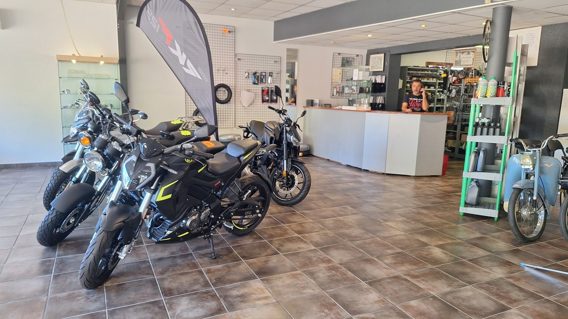 Intérieur de salle d'exposition de motos avec motos noires, comptoir de vente et accessoires exposés.