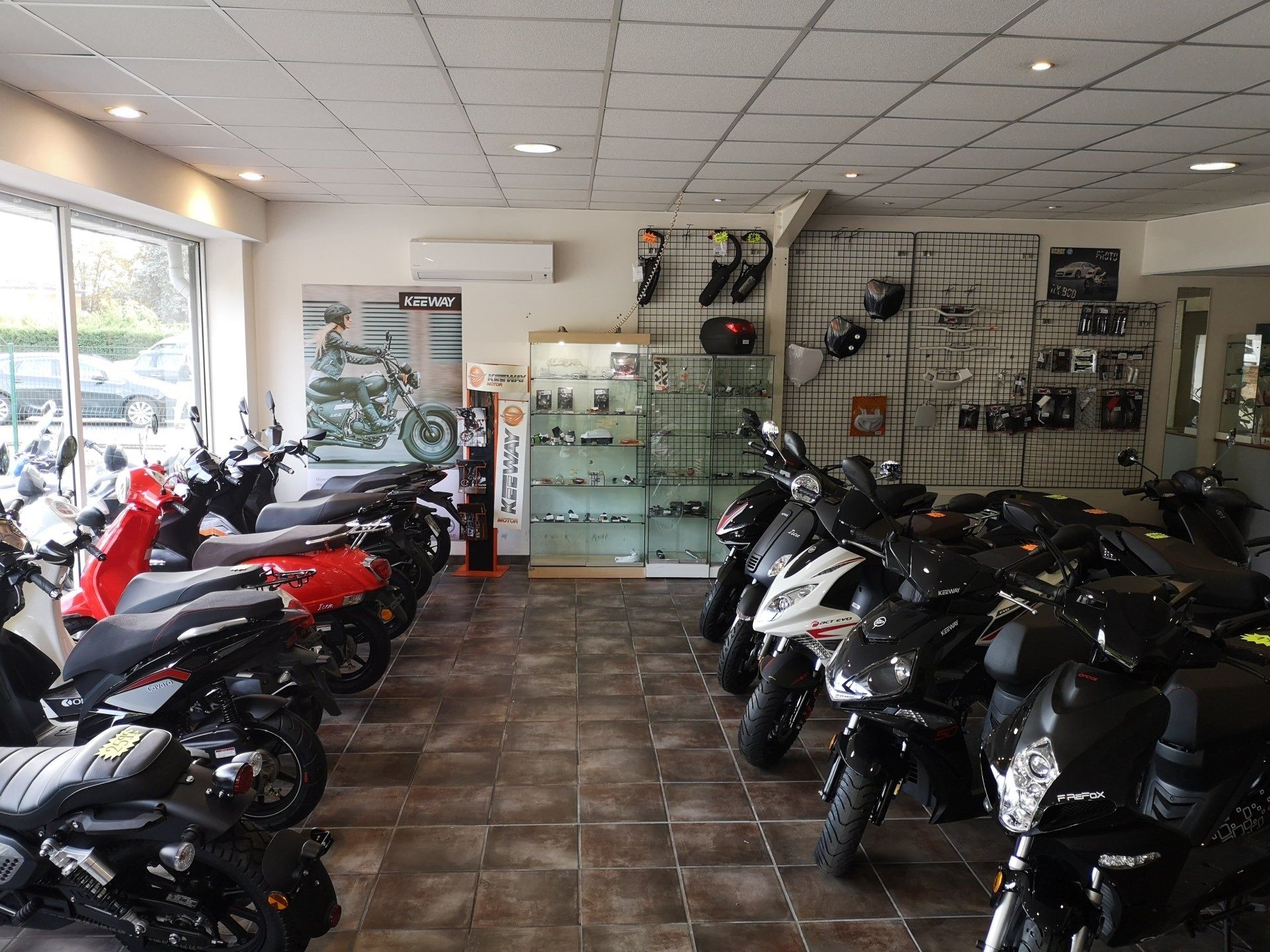Intérieur du showroom moto : scooters et accessoires exposés, avec éclairage et vitrines.