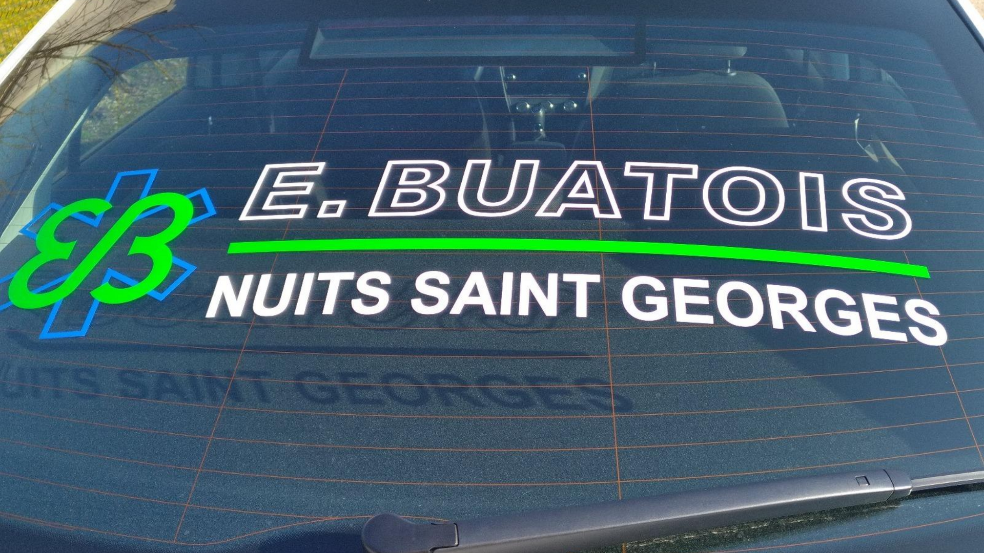 Lunette arrière blanche de voiture avec autocollant vert et bleu E. BUATOIS et NUITS-SAINT-GEORGES, symbole d'ambulance.