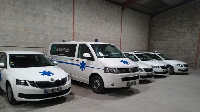 Une ambulance blanche et des voitures avec l'emblème de l'étoile bleue sont garées dans un garage.
