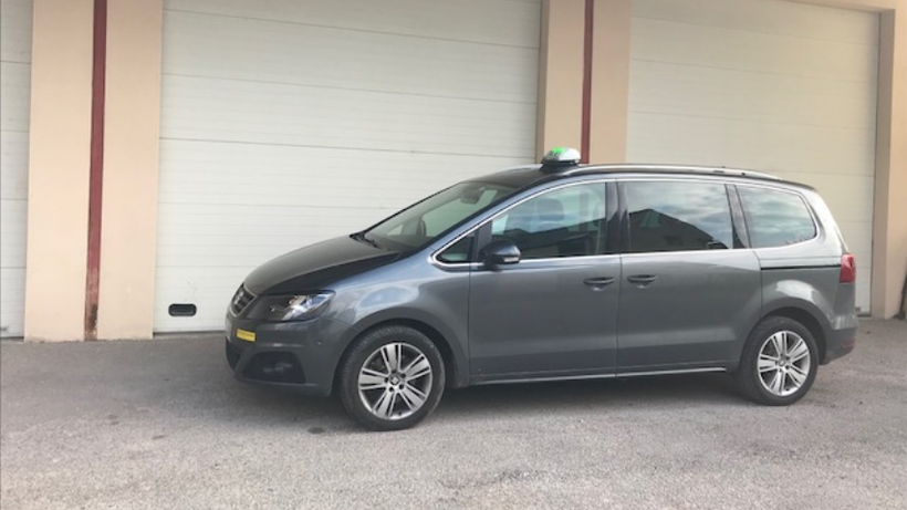 Un taxi gris foncé est garé devant des portes de garage blanches fermées.