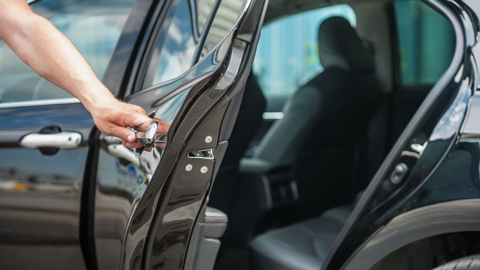 Une main ouvre une portière de voiture noire, révélant l'intérieur avec une personne sur le siège arrière.