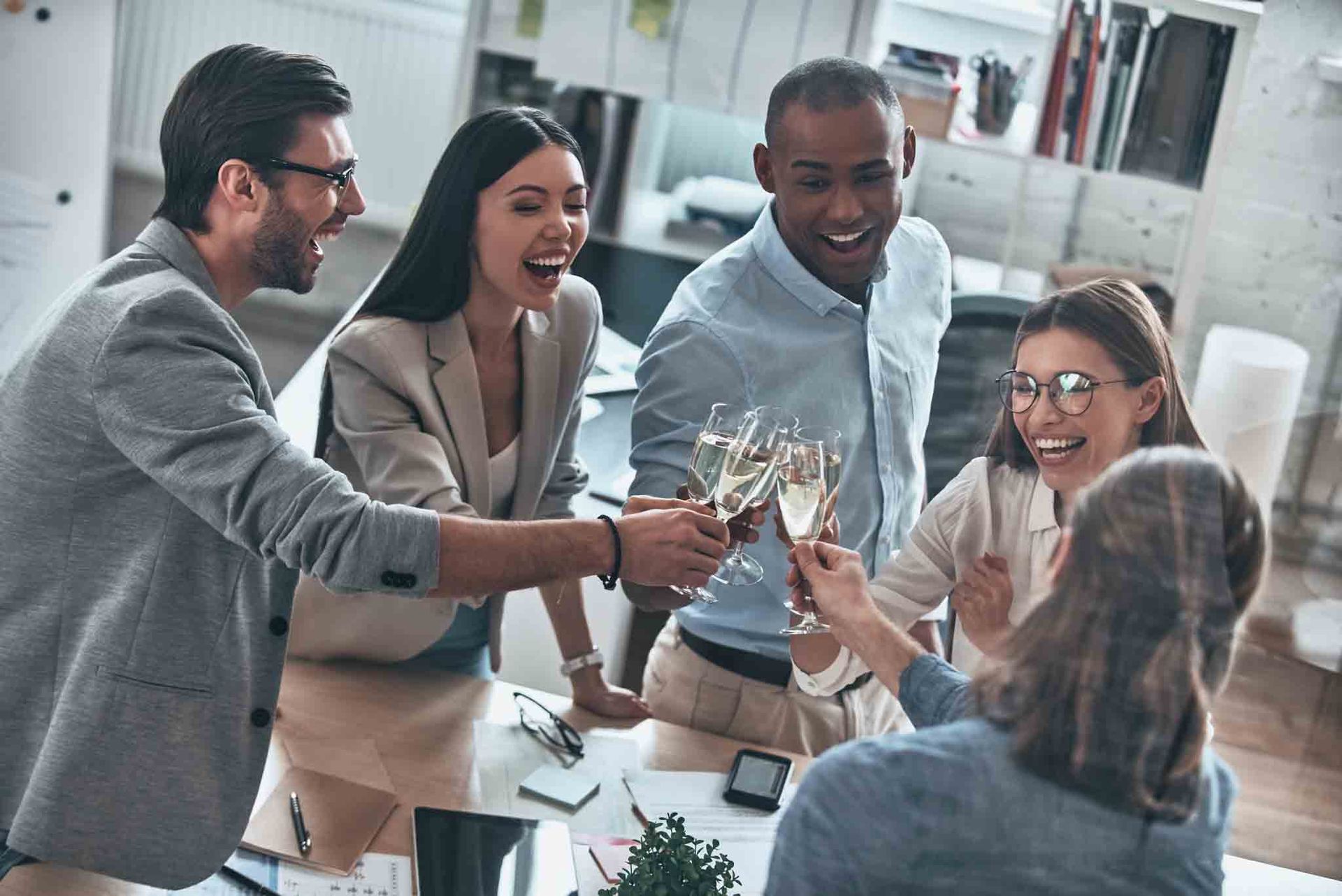 Equipo celebrando con copas de champán en una oficina, sonriendo y riendo.
