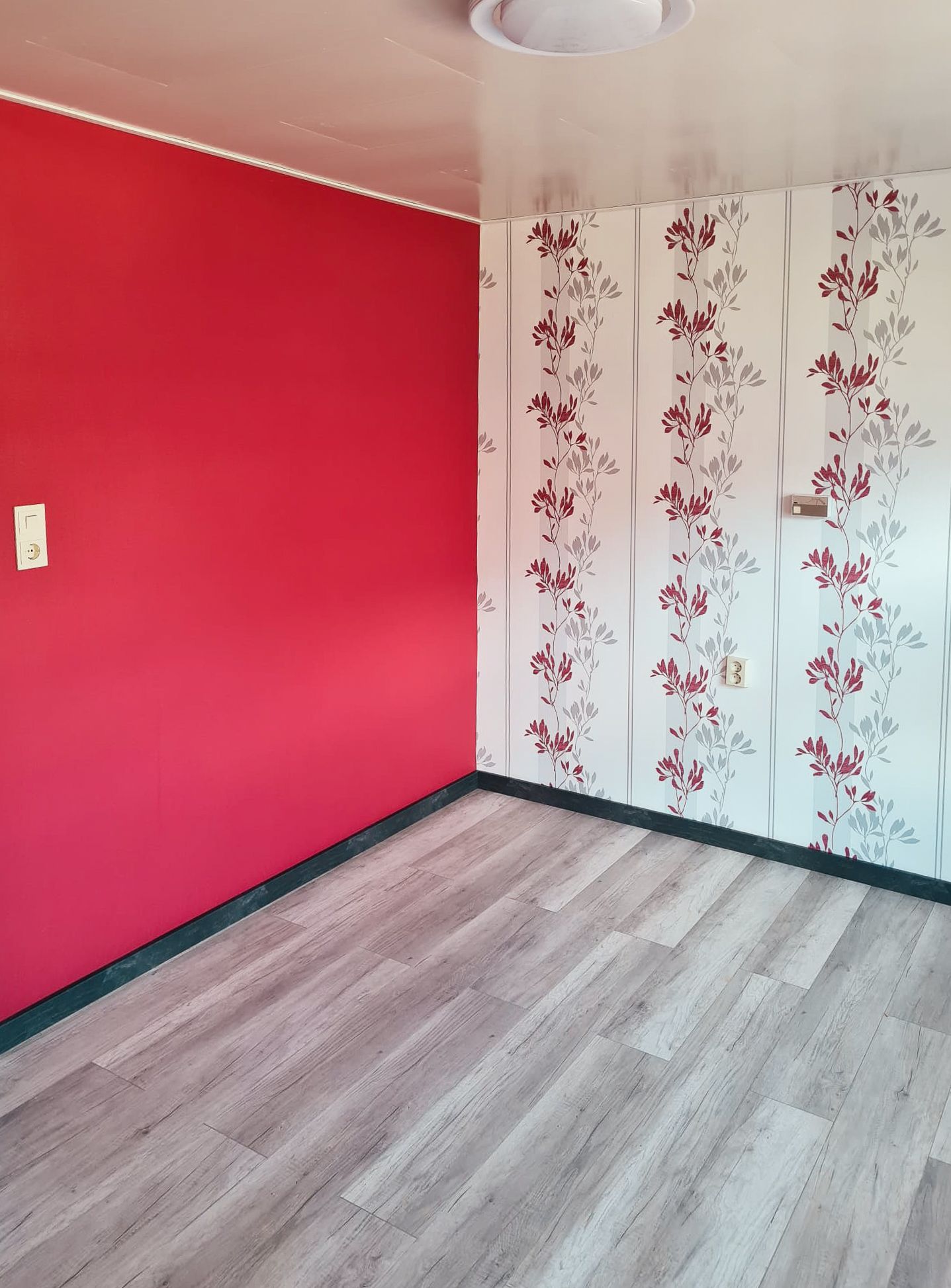 Ein leerer Raum mit einer roten Wand und einer geblümten Tapete