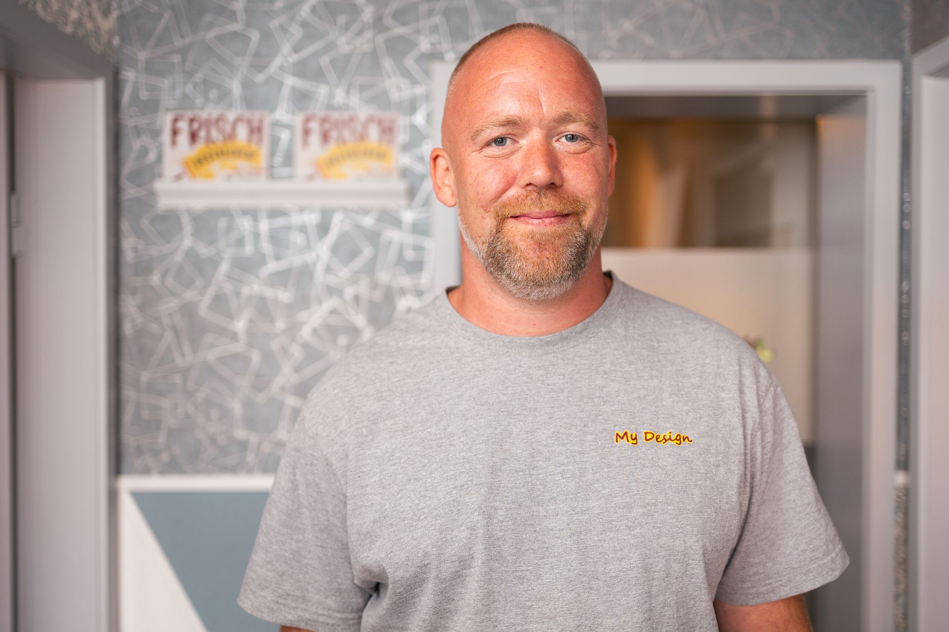 Ein Mann mit Bart trägt ein graues T-Shirt und lächelt.