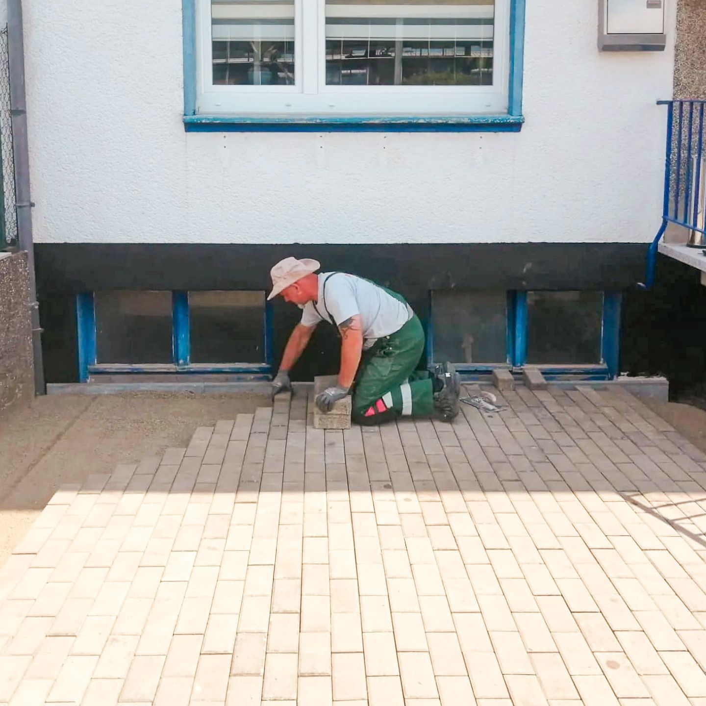 Ein Mann kniet auf einem Ziegelweg vor einem Gebäude