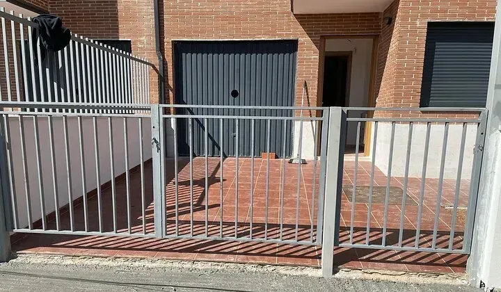 Una casa de ladrillo con una valla alrededor y una puerta de garaje.