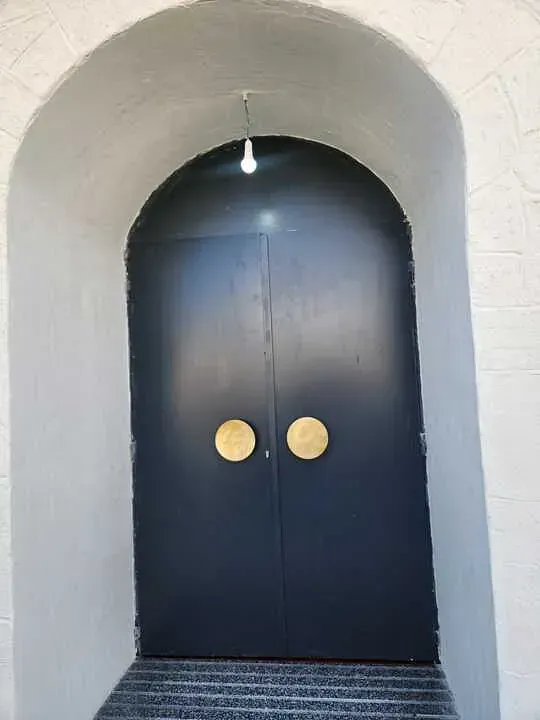 Una puerta negra con manijas doradas está en un arco blanco.
