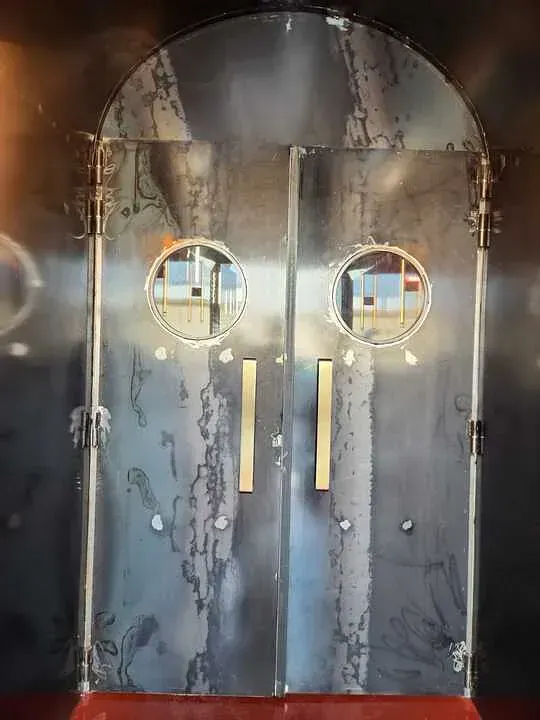 Un par de puertas de acero inoxidable con ventanas redondas y manijas doradas.