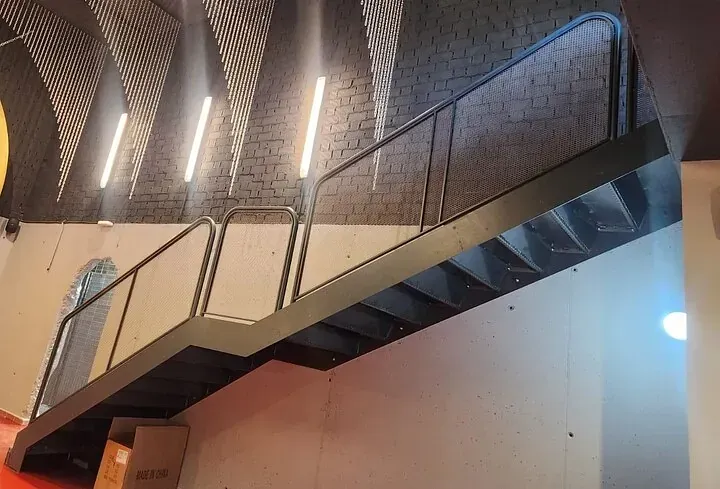 Una escalera de metal con barandilla en una habitación con una pared de ladrillo.