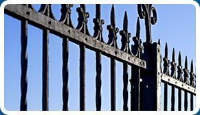 Un primer plano de una valla de hierro forjado con un cielo azul al fondo.