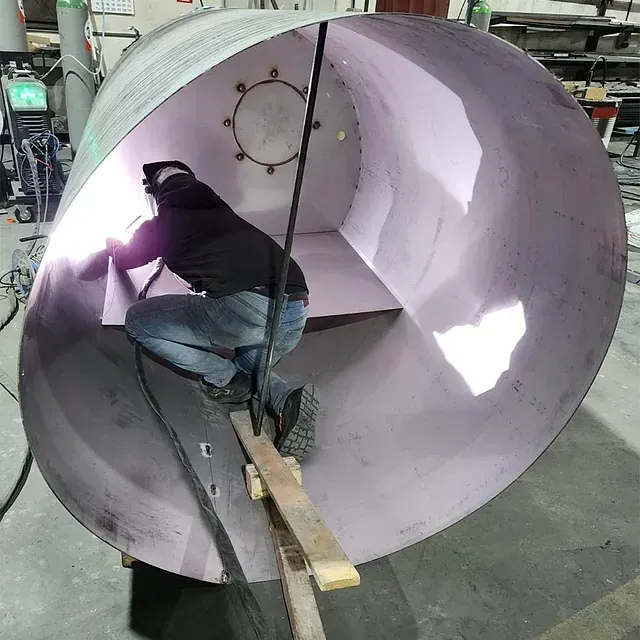 Un hombre está soldando un tubo grande en una fábrica.