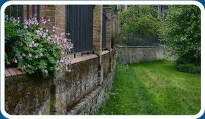 Una imagen de un jardín con un muro de piedra y una valla.