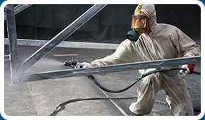 Un hombre que lleva una máscara de gas está rociando pintura sobre una estructura de metal.