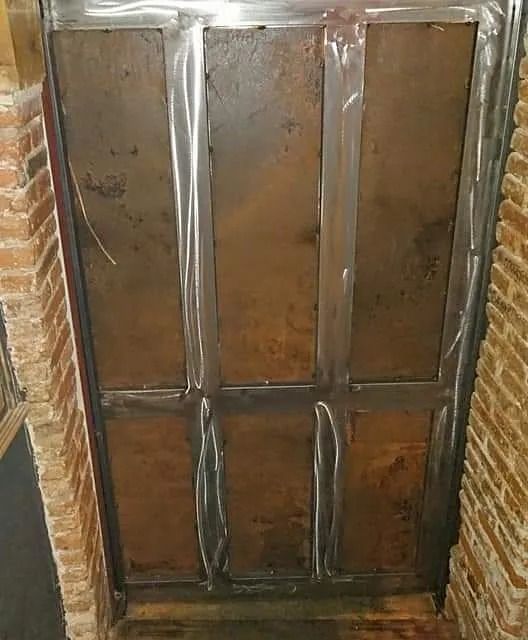 Una puerta de metal está en una habitación al lado de una pared de ladrillos.
