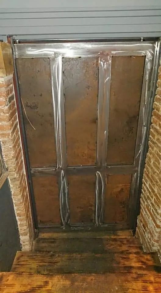 Una puerta de metal está colocada sobre un piso de madera al lado de una pared de ladrillos.