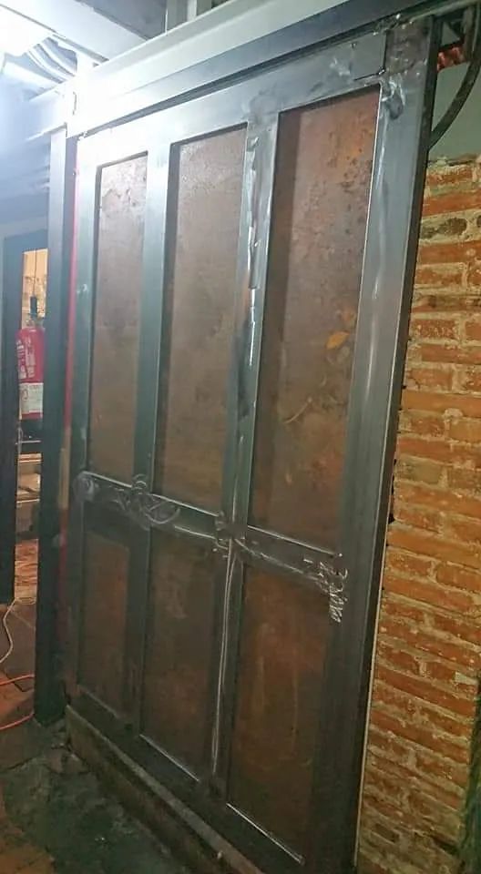 Una gran puerta de metal está al lado de una pared de ladrillos.