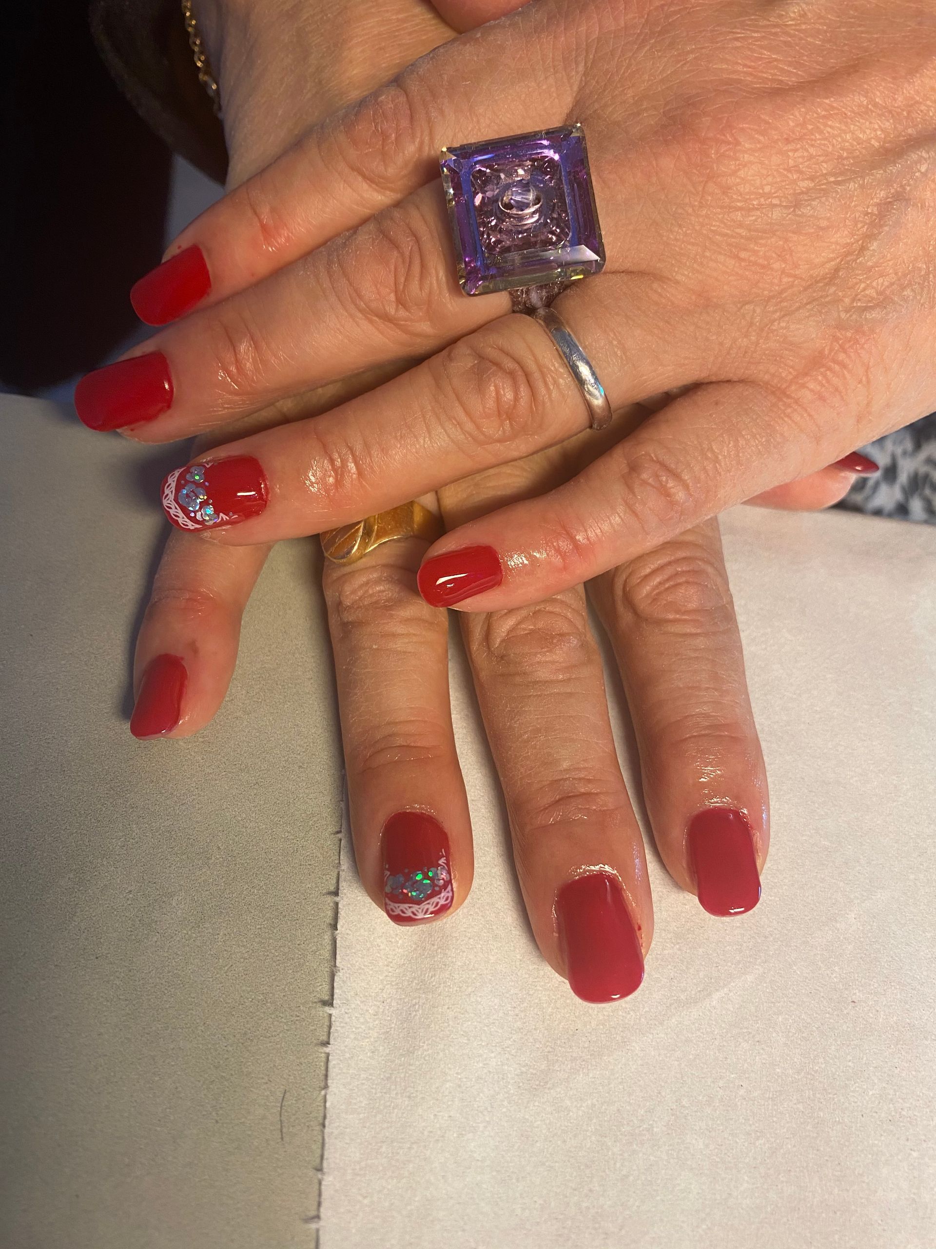 Des mains aux ongles vernis en rouge et portant des bagues reposent sur une surface claire.