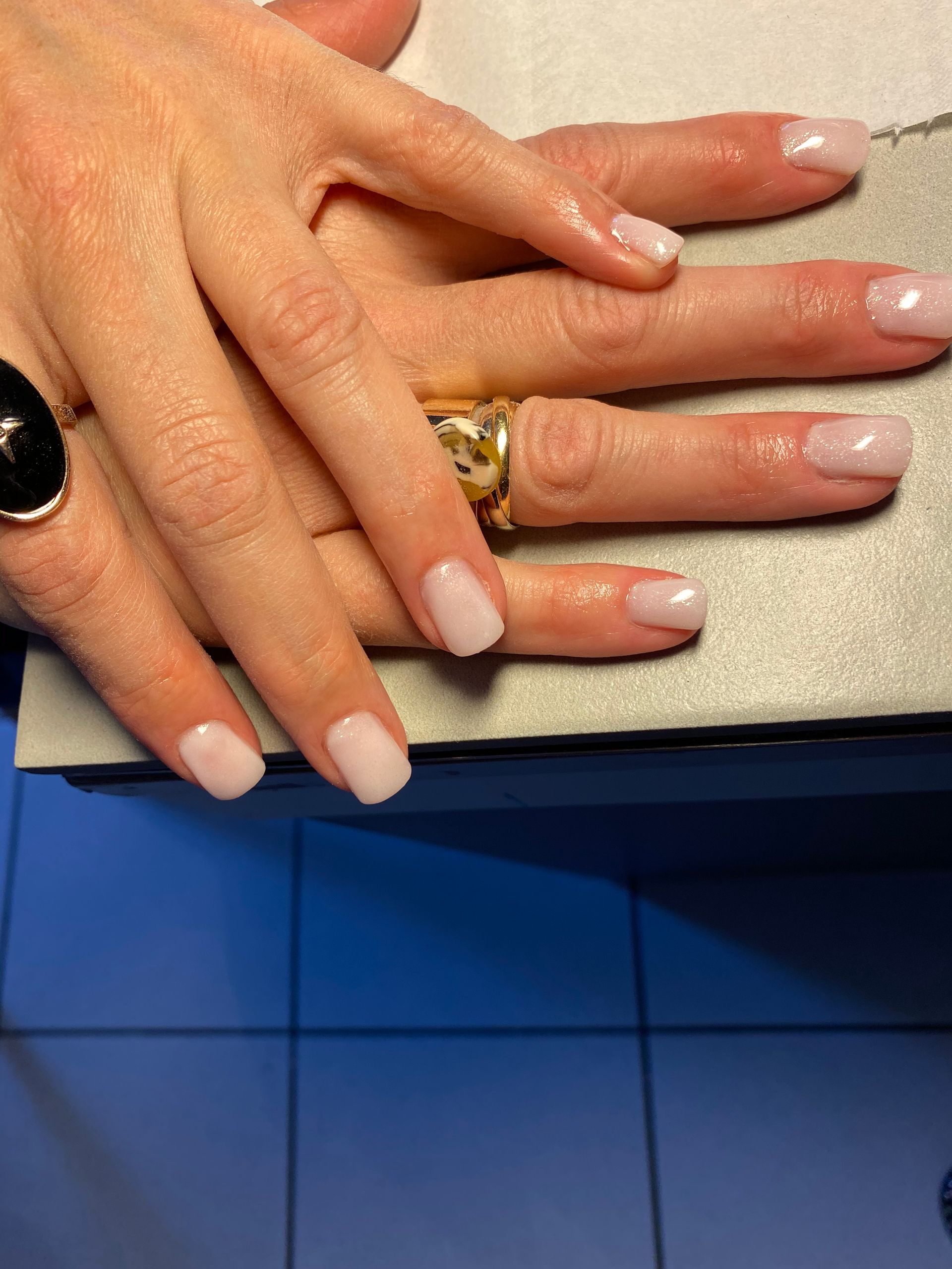 Deux mains aux ongles manucurés rose pâle posées sur un comptoir bleu.