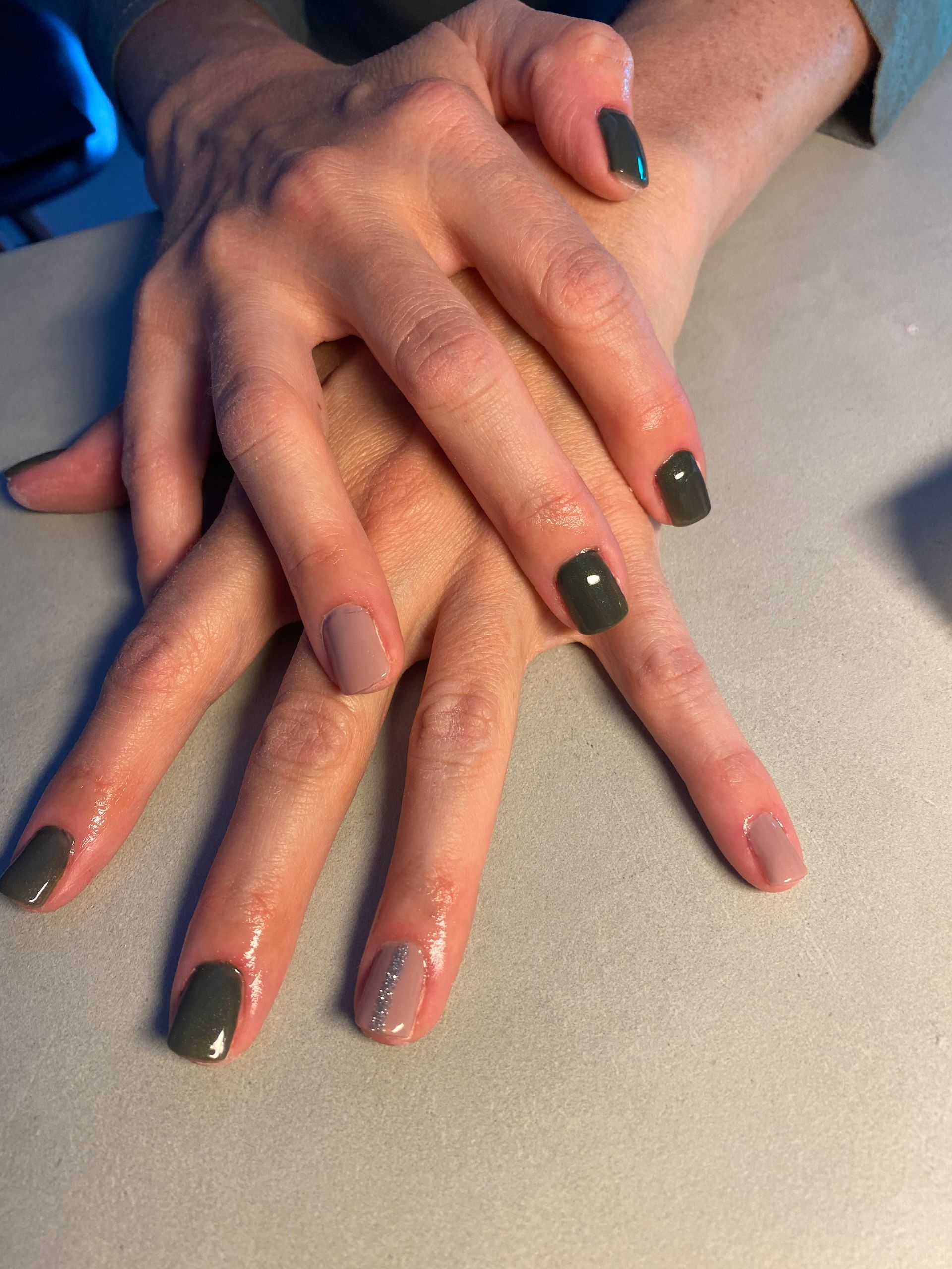 Des mains aux ongles vernis vert foncé, jointes sur une table claire.