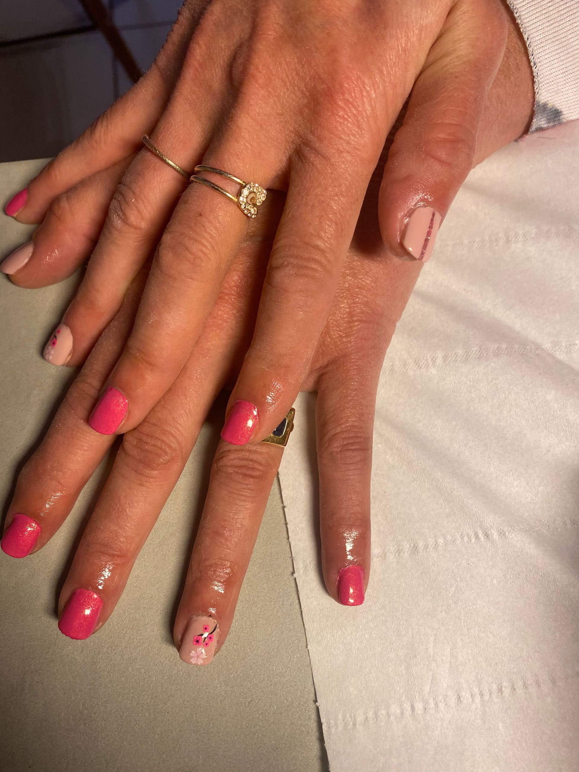 Deux mains aux ongles roses manucurés et aux bagues en or posées sur un tissu blanc.