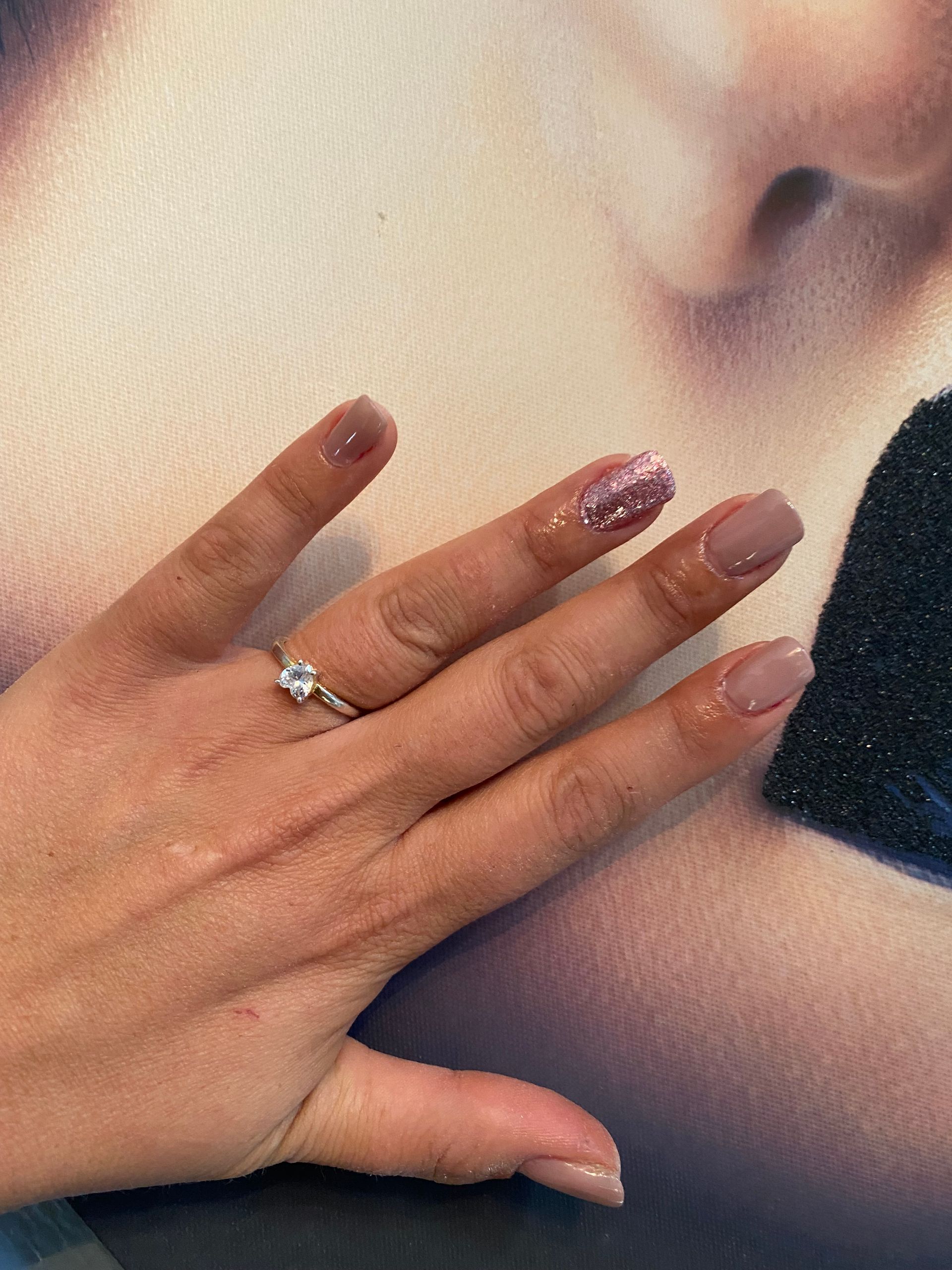 Main ornée d'une bague en argent posée sur une épaule nue, dévoilant des ongles nude et mauve pailleté.