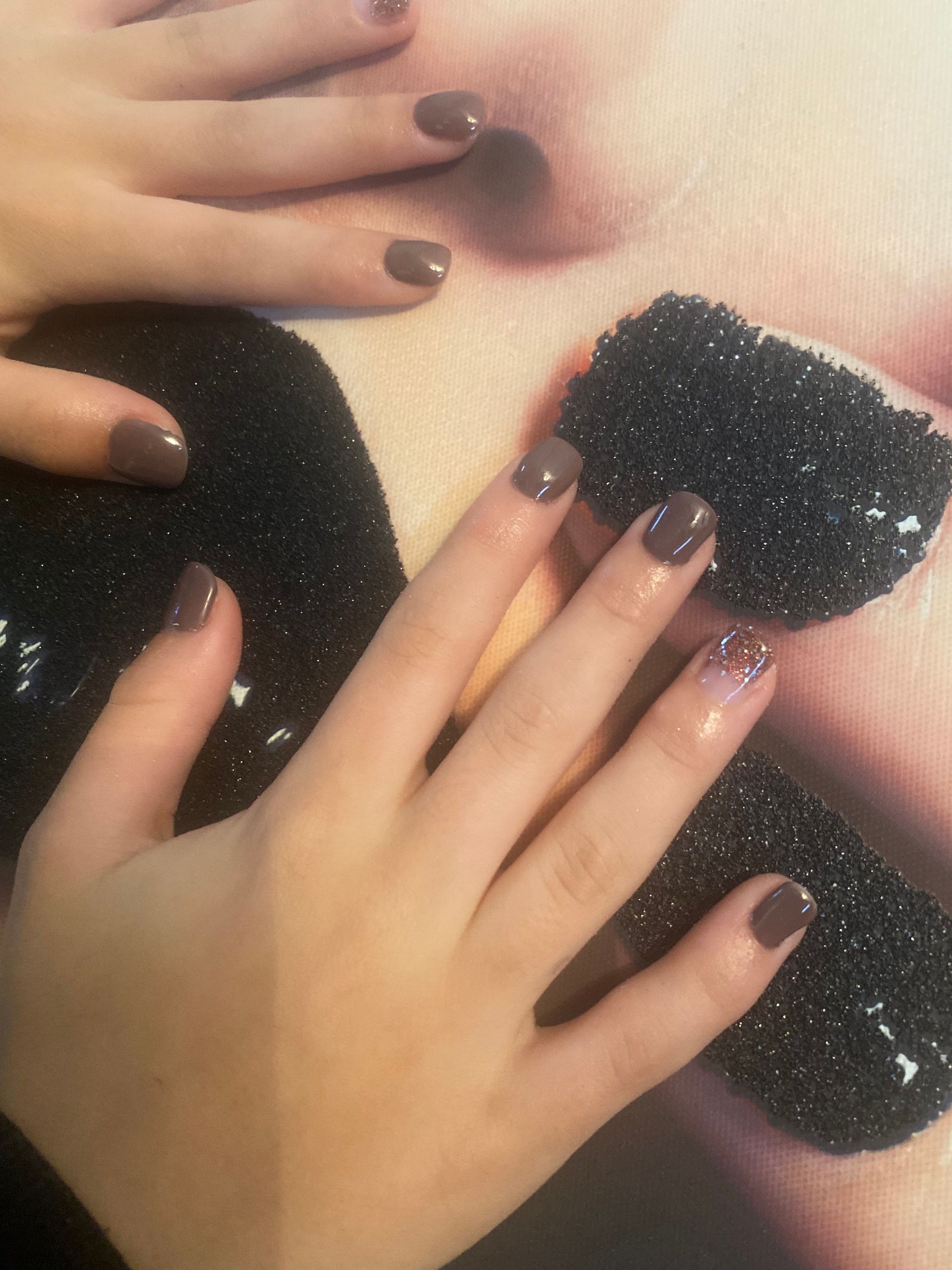 Des mains aux ongles vernis foncés posées sur un tissu noir à paillettes.