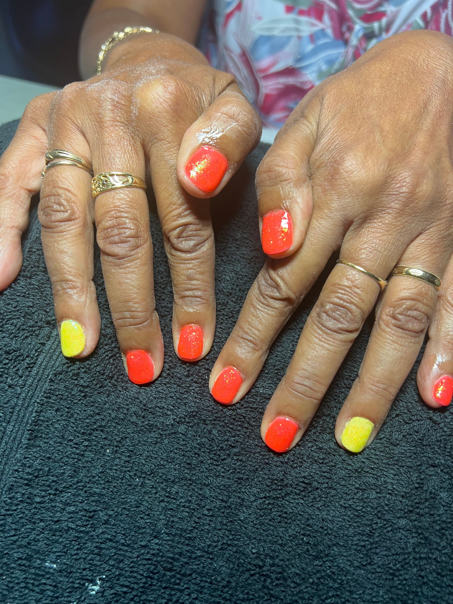 Des mains aux ongles orange vif et jaunes posées sur un tissu bleu foncé.