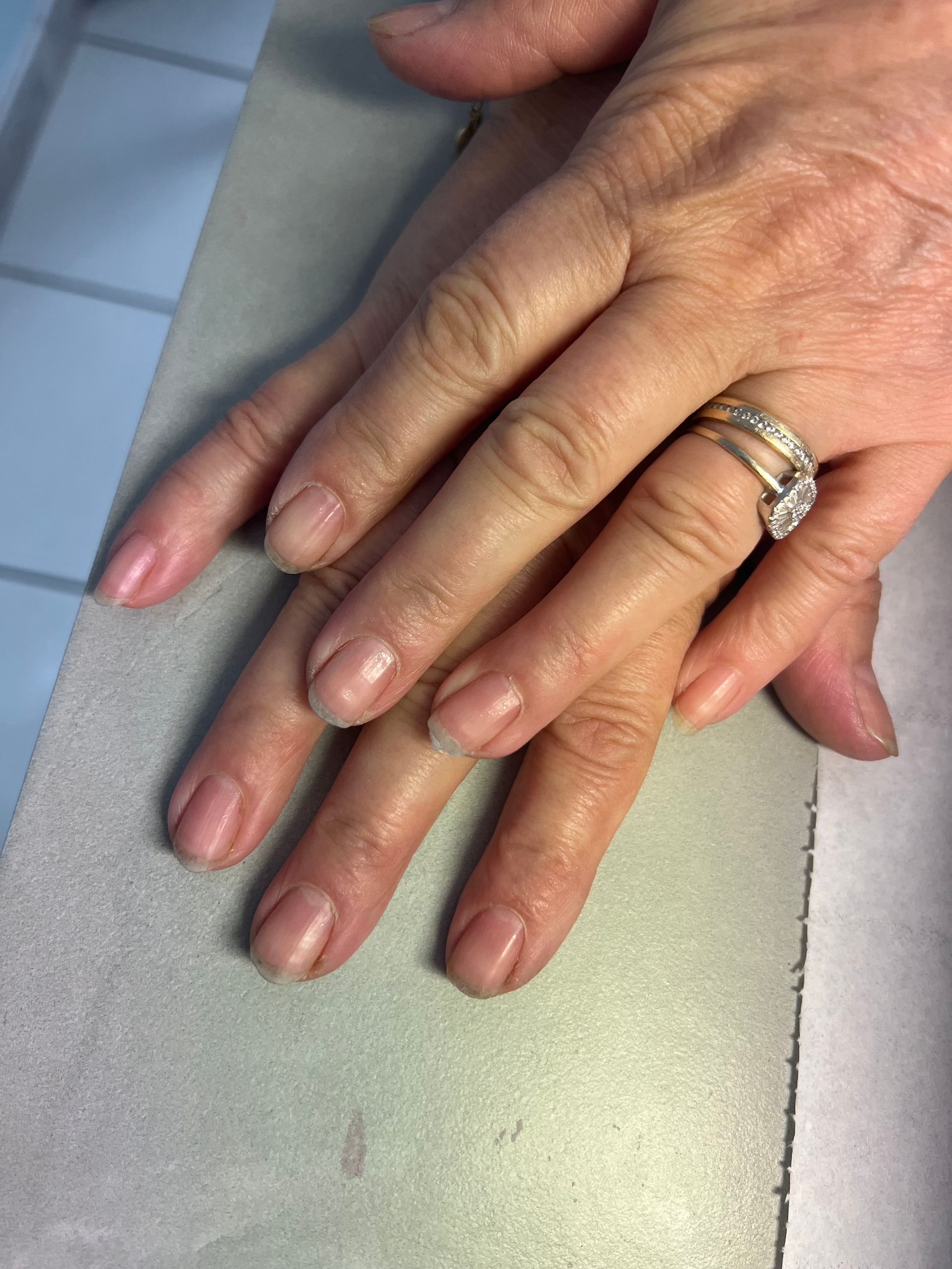 Des mains posées sur une table gris clair, l'une d'elles portant une bague en argent et du vernis à ongles rose.