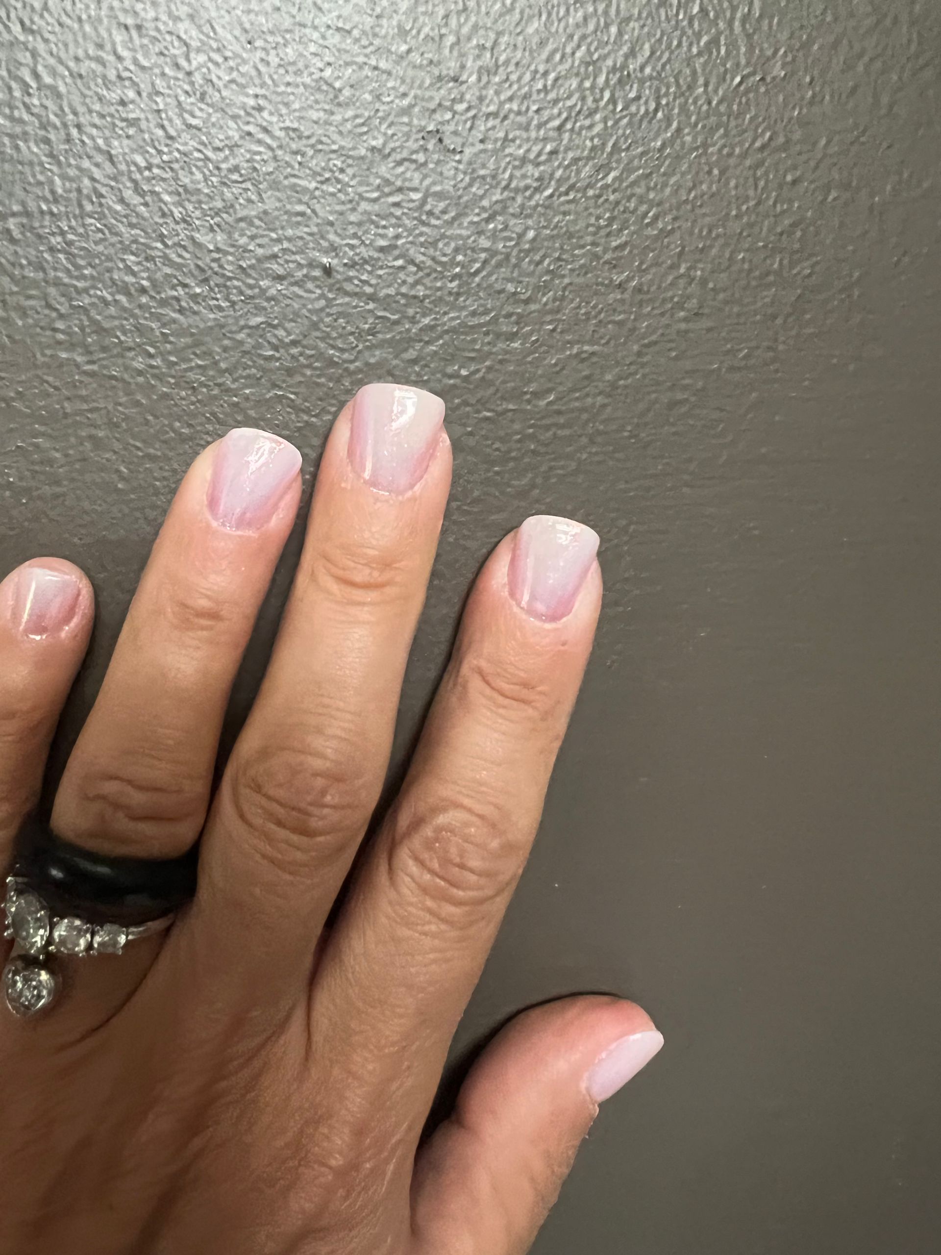 Main avec manucure rose pâle et bagues noires sur fond gris