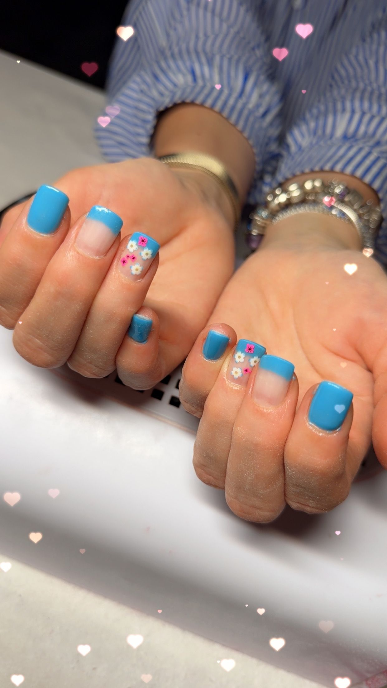 Des mains aux ongles vernis d'un bleu vif et aux ongles accentués de paillettes reposent côte à côte sur une surface blanche.