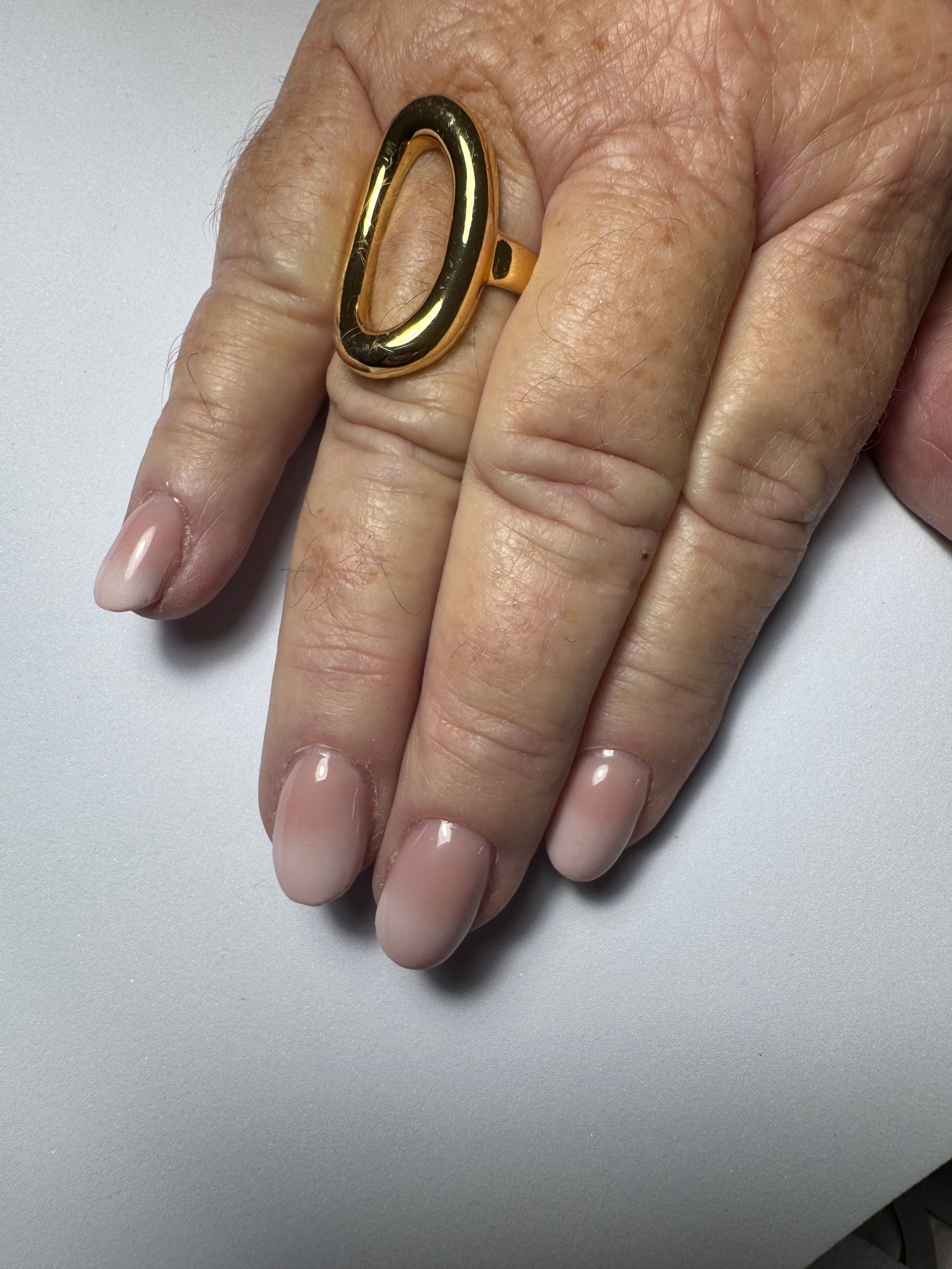 Main portant une bague en or posée sur une surface blanche