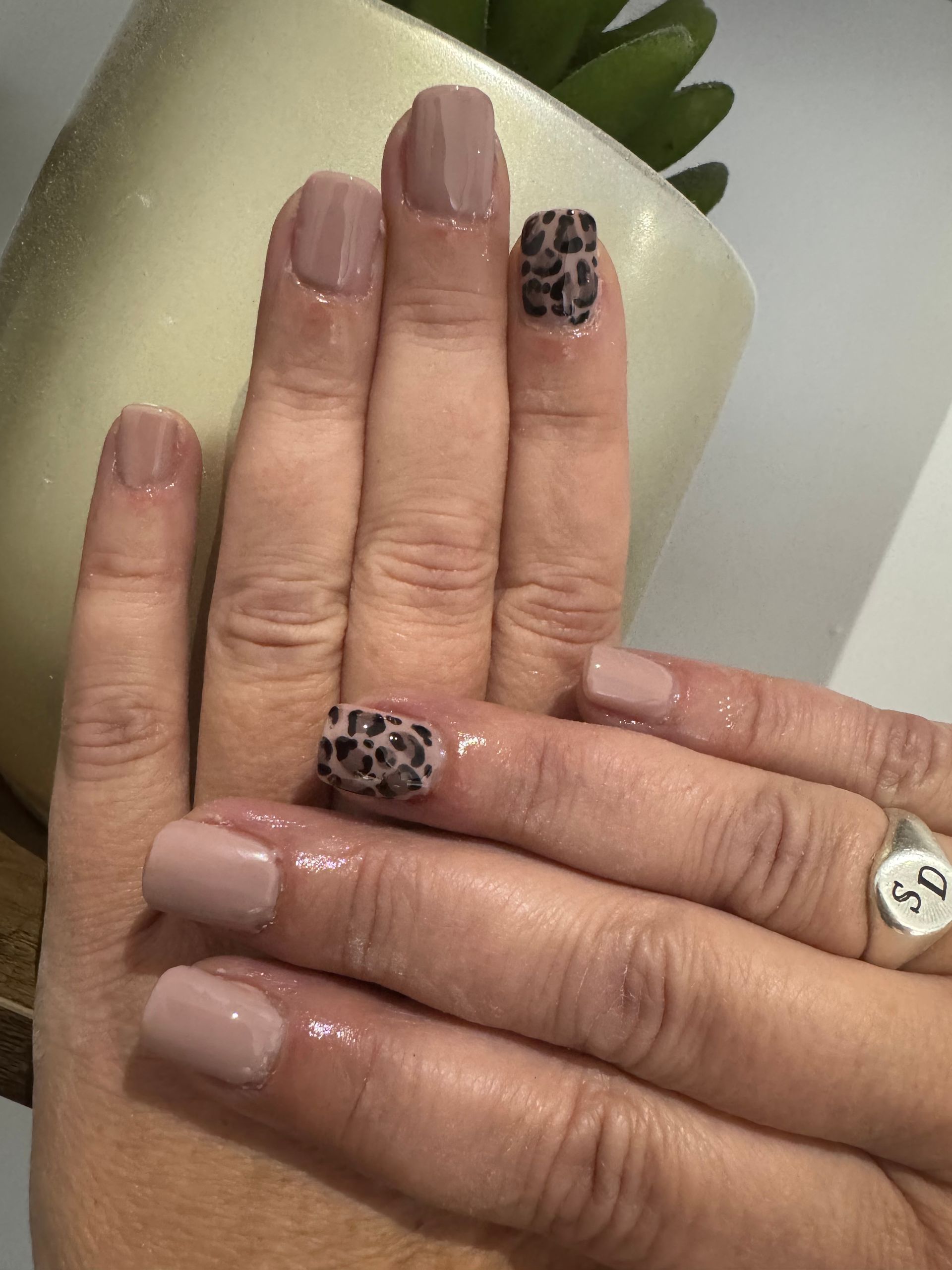 Gros plan sur des mains aux ongles nude et imprimé léopard, tenant une tasse blanche.