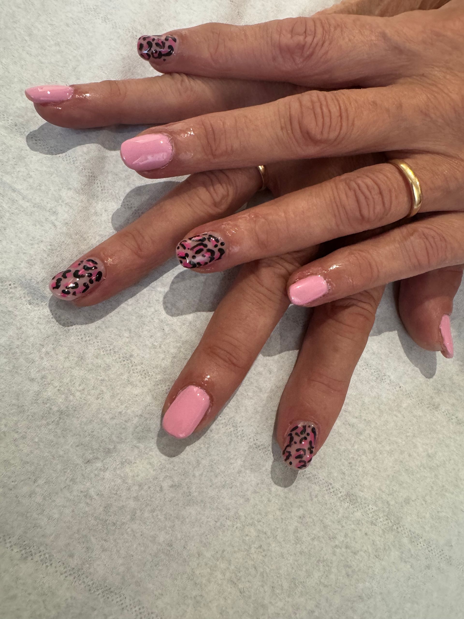 Mains aux ongles manucurés roses et à imprimé léopard sur une surface gris clair