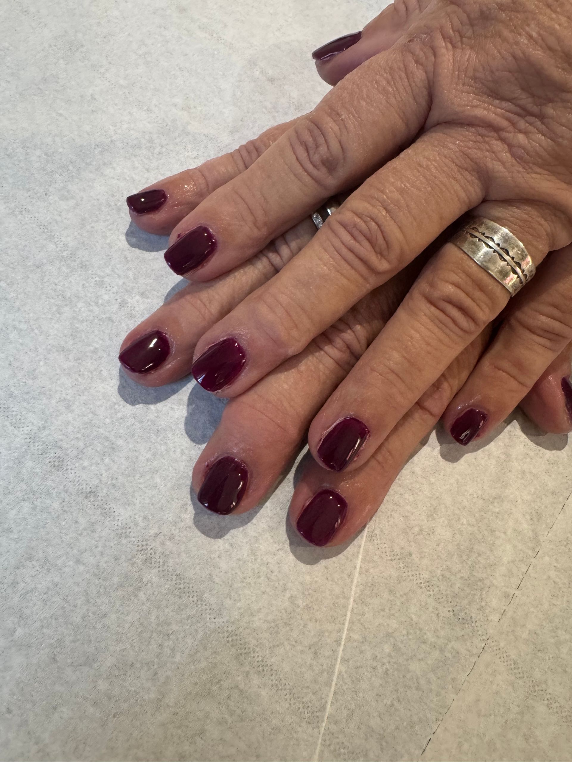 Des mains aux ongles vernis d'un bordeaux foncé et une bague en argent posées sur une surface claire